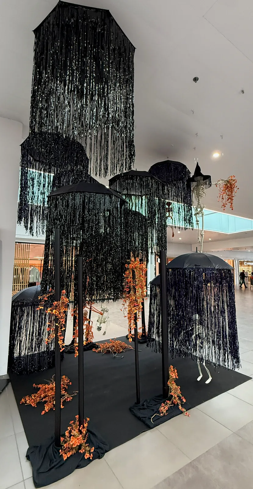 Forêt de structures à franges noires et feuillage orange dans une galerie commerciale